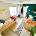 Bright shared kids bedroom with twin natural wood beds, emerald green accent wall, colorful boho rug, canopy reading nook, toys and houseplants