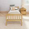 Farmhouse bedroom with wooden single bed, neutral bedding, knitted throw pillow, wooden nightstand and lamp against a white shiplap wall
