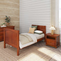 Cozy farmhouse bedroom interior with wooden twin bed and nightstand, neutral layered bedding, horizontal shiplap accent wall, woven jute rug, potted plants, linen curtains and bedside lamp