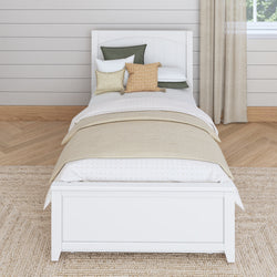 Single bed with white frame and layered pillows in a cozy bedroom setting.