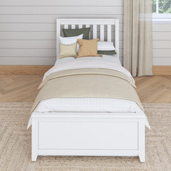 White wooden bed with beige bedding and decorative pillows in a cozy bedroom setting.