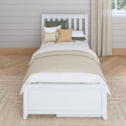 Single white bed with layered bedding and pillows in a cozy, neutral-toned bedroom.