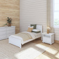 Cozy neutral bedroom with white wooden twin bed, beige shiplap and woven grasscloth accent wall, white dresser, textured rug, potted plants and natural light