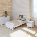 Neutral modern farmhouse bedroom with white wooden twin bed, beige shiplap and grasscloth accent walls, woven jute rug, white dresser, bedside lamp and potted plants