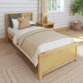 Cozy neutral farmhouse bedroom with wooden bed frame, beige layered bedding and textured throw pillows, nightstand lamp, shiplap wall, sunlit window and woven jute rug