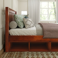 Wooden bed frame with decorative pillows and cozy blanket in a sunlit bedroom.