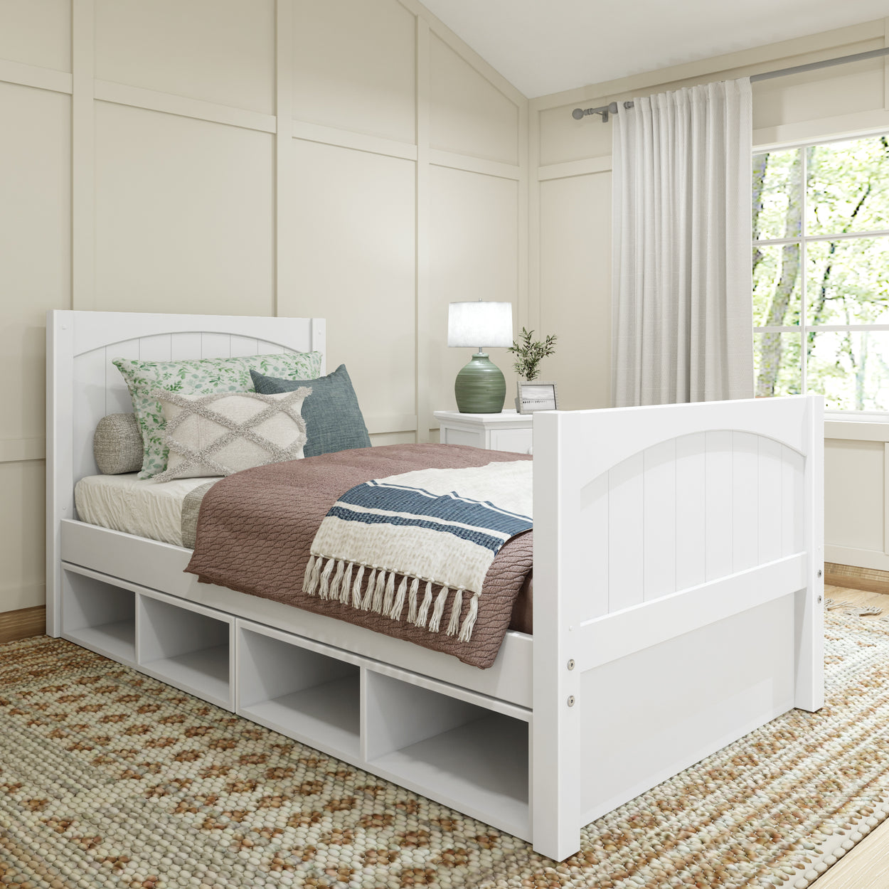 White wooden bed with storage drawers in cozy bedroom featuring decorative pillows, soft bedding, and a side table lamp.