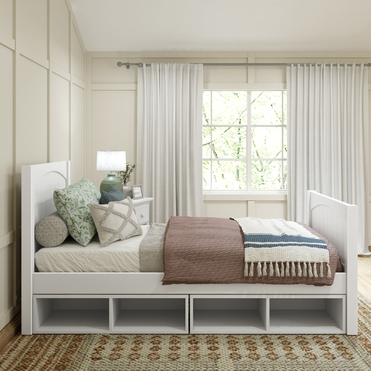 Modern bedroom with a white wooden daybed featuring storage shelves, cozy pillows, and layered bedding in neutral tones, complemented by natural light from a large window.