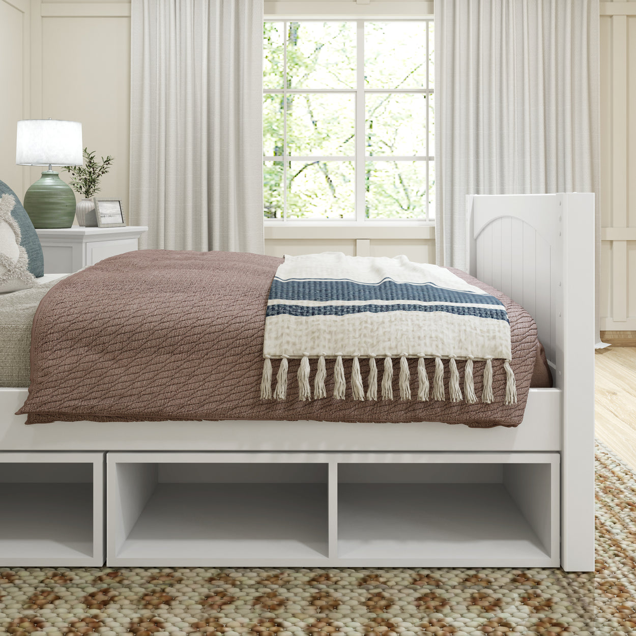Cozy bedroom interior with a stylish brown bedspread and decorative throw on a bed with storage shelves, beside a white nightstand with a lamp and framed picture.