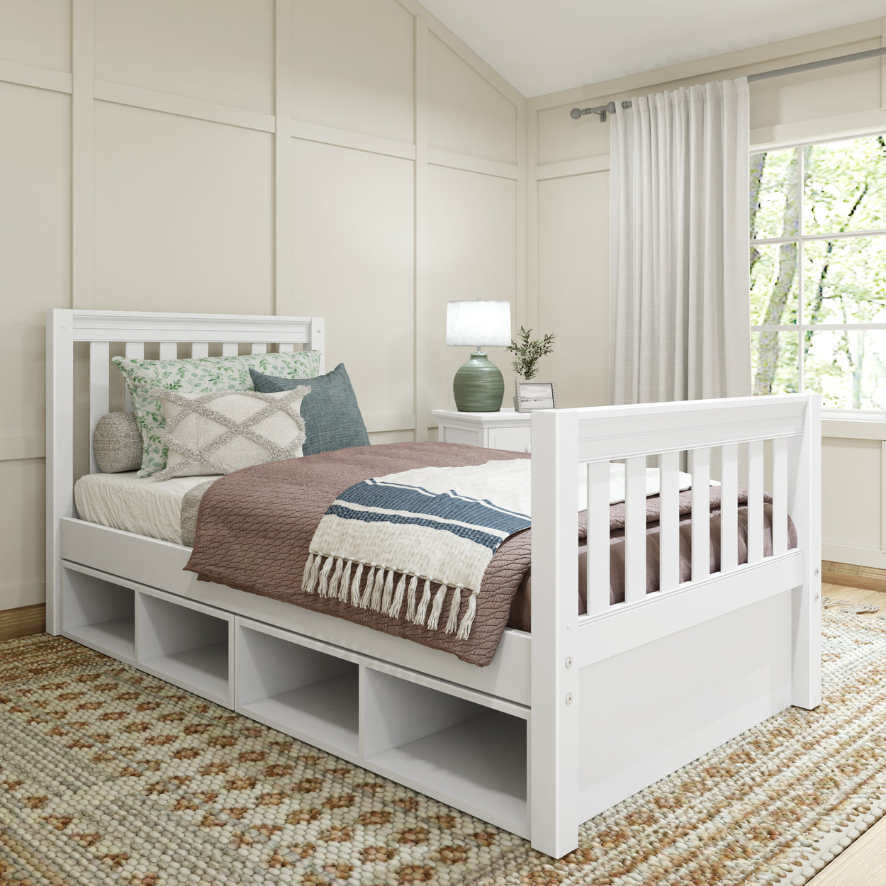 Cozy bedroom with a white wooden daybed featuring storage drawers, decorative pillows, and a warm brown blanket, near a window and a lamp on a side table.