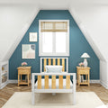 Cozy attic bedroom with teal accent wall, white wooden bed with natural slats, matching nightstands, bamboo blinds, pastel wall art and table lamp on herringbone hardwood floor
