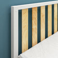 Close-up of modern headboard with white frame and vertical light wood slats against a teal wall, corner of bed mattress visible