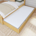 Wooden bed frame with pull-out trundle bed and white mattress in cozy bedroom setting.