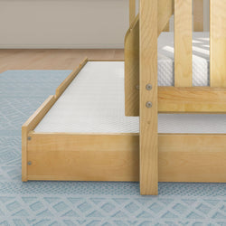 Wooden toddler bed with pull-out trundle on blue patterned rug in bright bedroom.