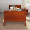 Orange wooden bed with neutral pillows, bedside table and lamp, white shiplap wall and woven jute rug in farmhouse bedroom