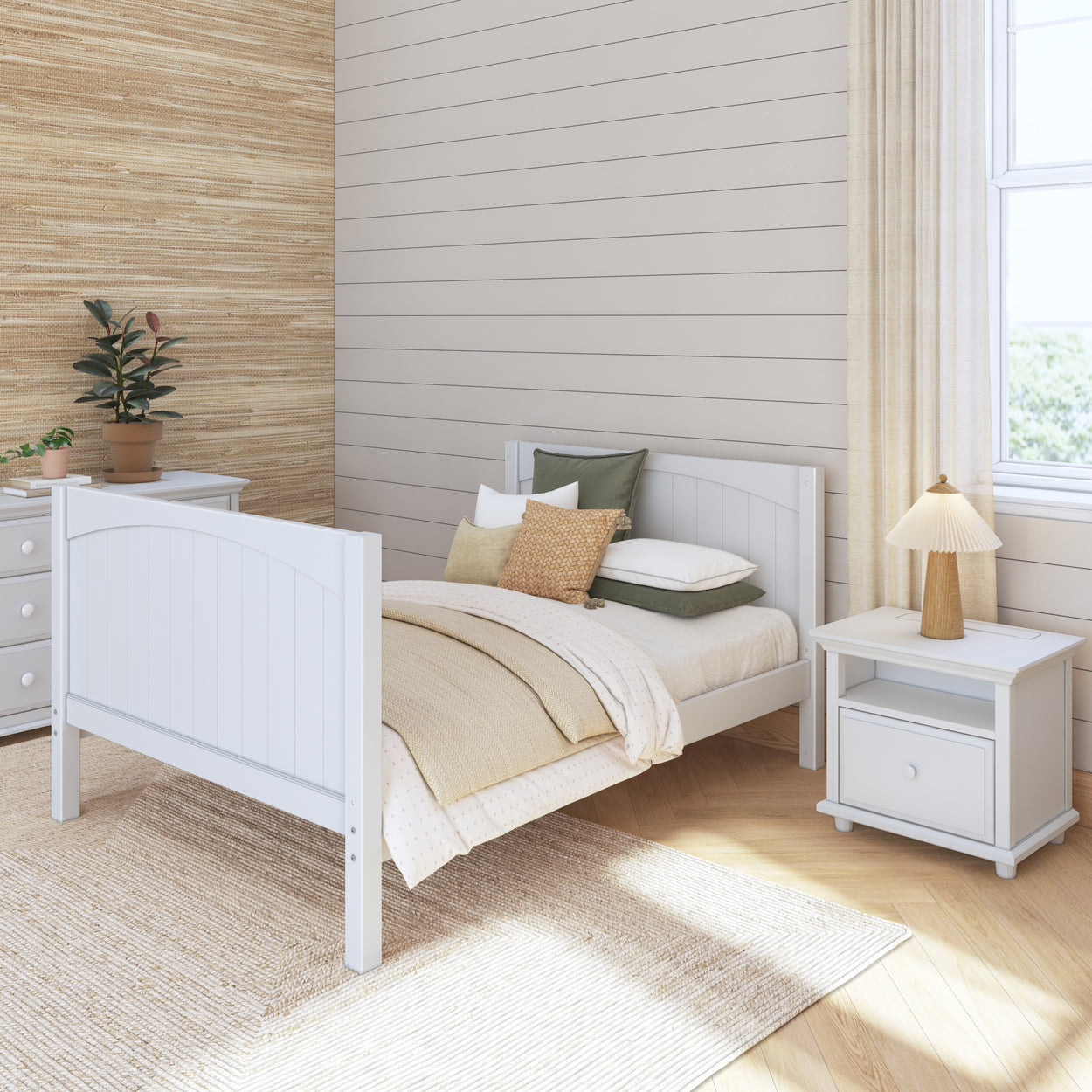 Cozy bedroom with white wooden bed, beige bedding, and a nightstand with a lamp, featuring natural light from a large window.