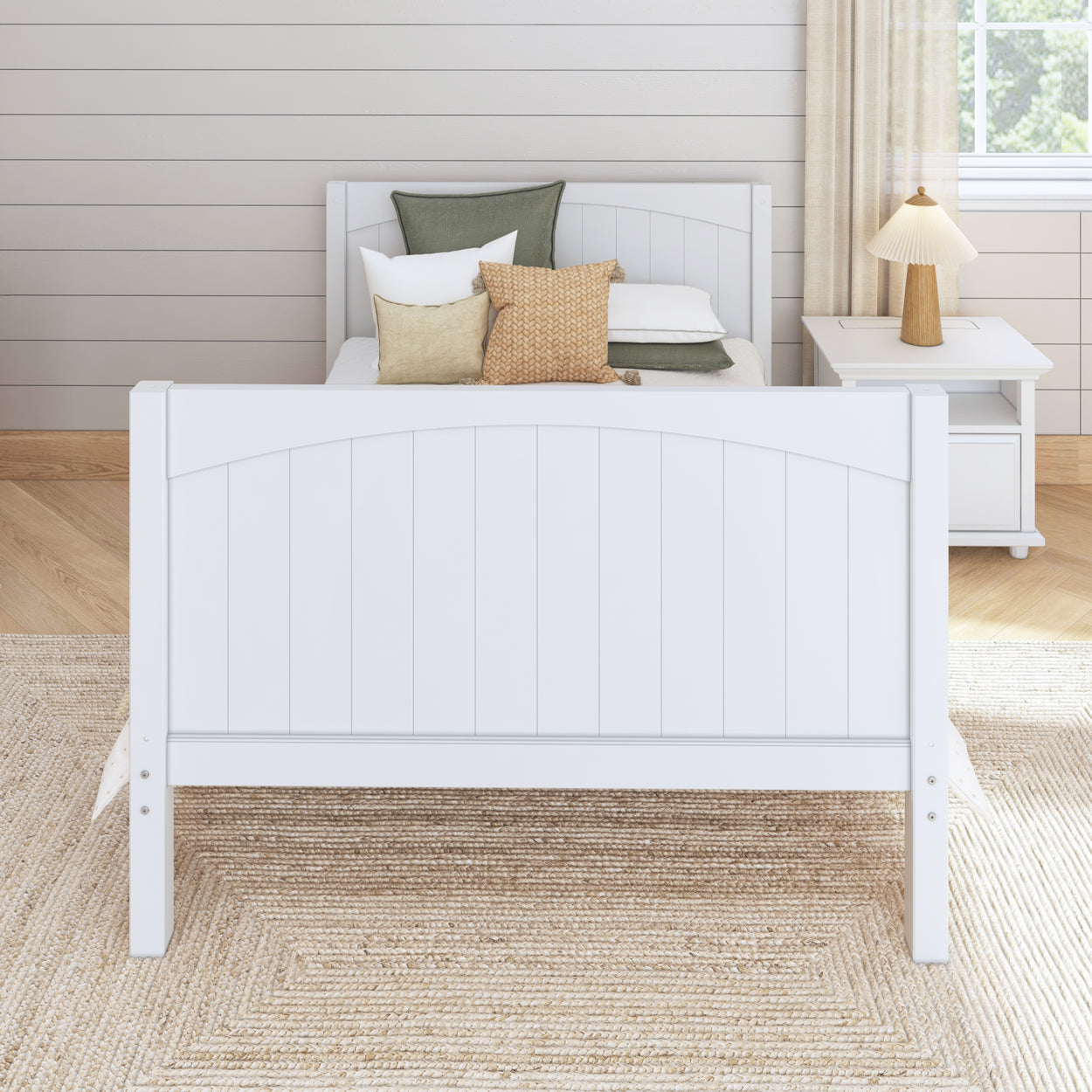 White wooden bed with decorative pillows in a cozy bedroom with a nightstand and lamp.