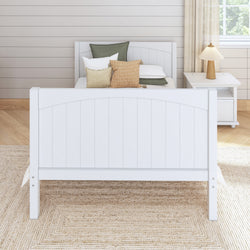 White wooden bed with decorative pillows in a cozy bedroom with a nightstand and lamp.