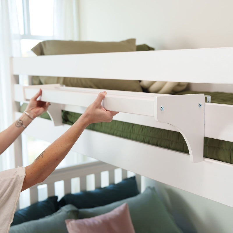 Close-up of hands installing white wooden bunk bed safety rail above green bedding in a modern kids' bedroom