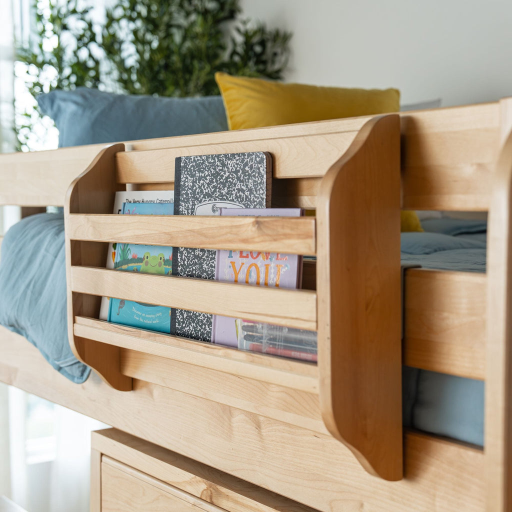 Maple-finish wooden bunk bed with built-in bedside bookshelf filled with children's books, blue bedding and a yellow pillow in a modern kids' bedroom
