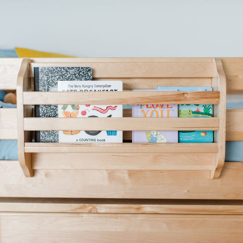 Light maple bedside book rack attached to children's bed holding colorful board books like The Very Hungry Caterpillar.