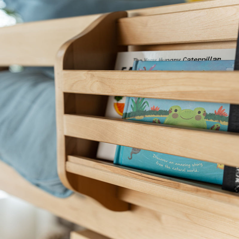 Wooden kids' bed with built-in bedside bookshelf holding colorful children's picture books and blue bedding, nursery storage solution