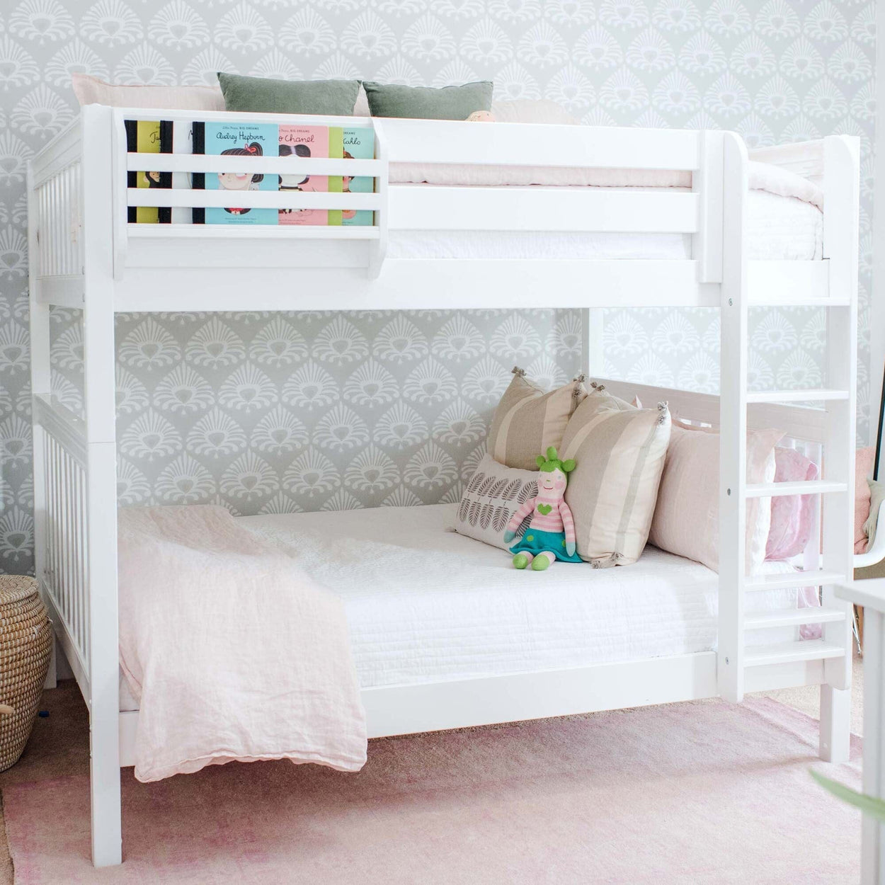White wooden bunk bed in pastel girls' bedroom with pink bedding, decorative pillows, ladder, kids' books and stuffed toy