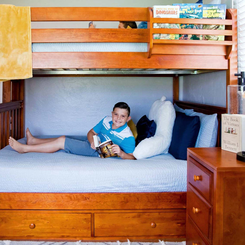 Child reading a book on the lower wooden bunk bed in a cozy kids' bedroom with blue bedding, under-bed storage drawers and nightstand