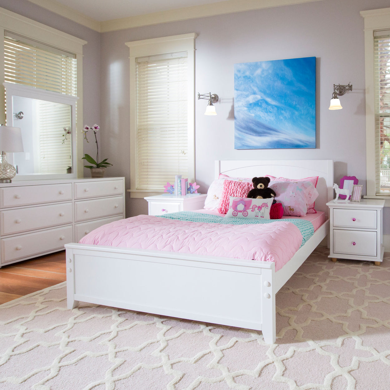 Bright modern children's bedroom with white furniture, pink bedding, and wall art, featuring a plush teddy bear and decorative accents.