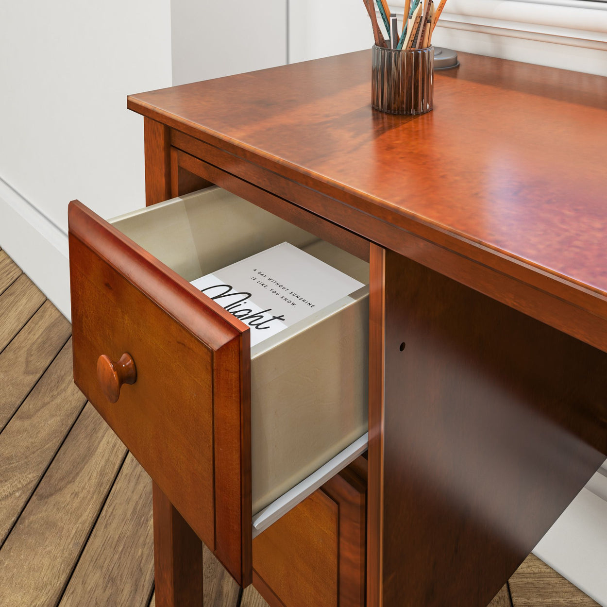 Open wooden desk drawer with book and cup of pencils, organized office space.