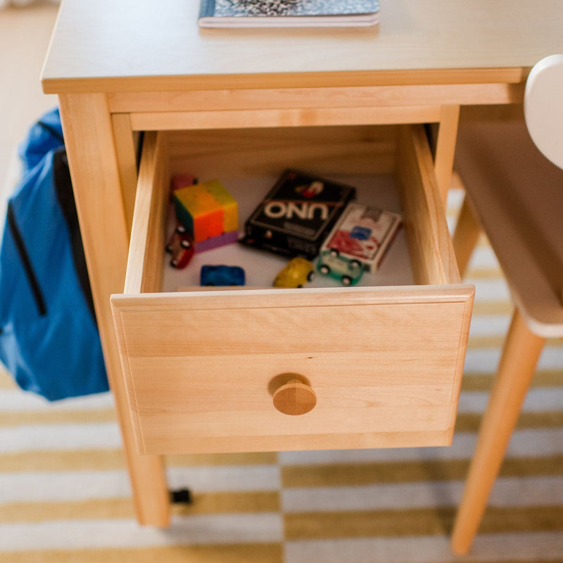 Open light-wood desk drawer with children's toys — toy cars, a colorful cube and UNO cards, ideal kids' desk storage