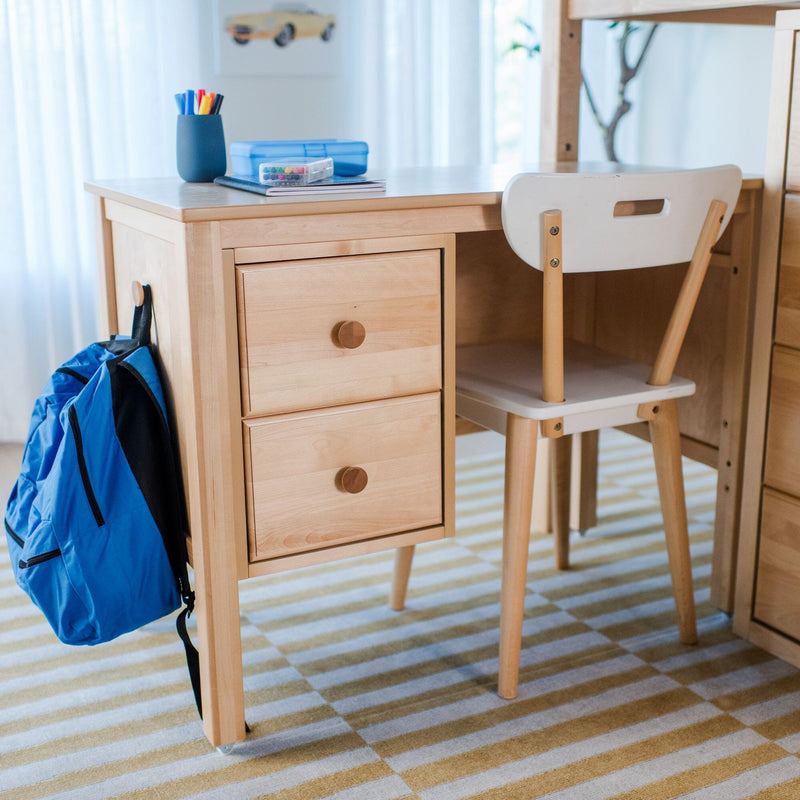 Wooden kids study desk and chair with blue backpack, pens and crayons on tabletop in an organized home learning space