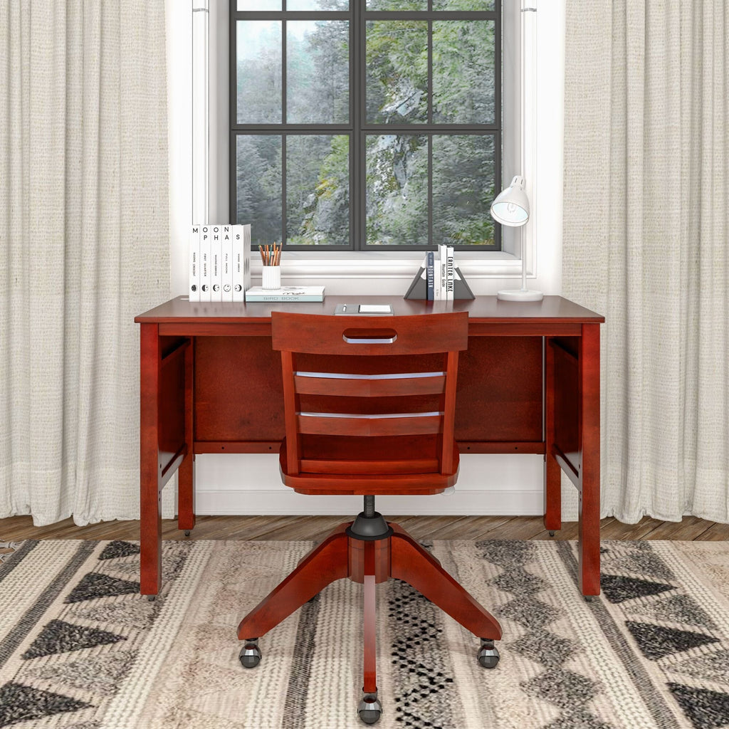 Cherry wood home office desk and matching swivel chair by window with desk lamp, books, neutral curtains and patterned rug