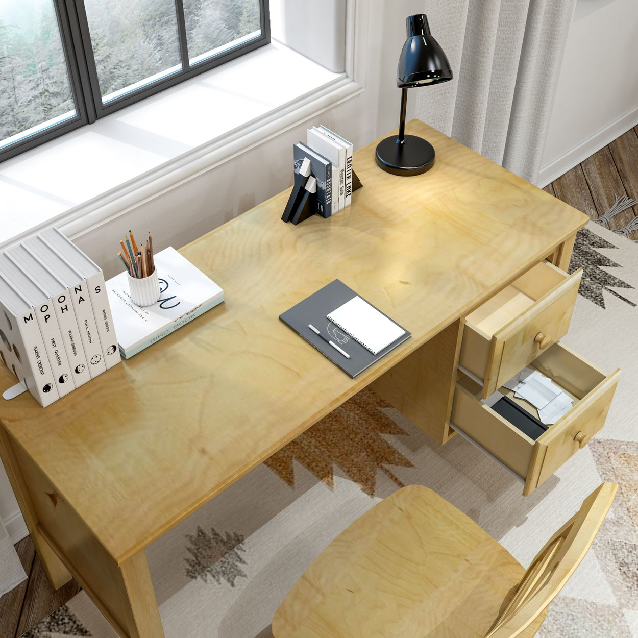Wooden office desk with a black lamp, open drawers, books, and pencils near a window.
