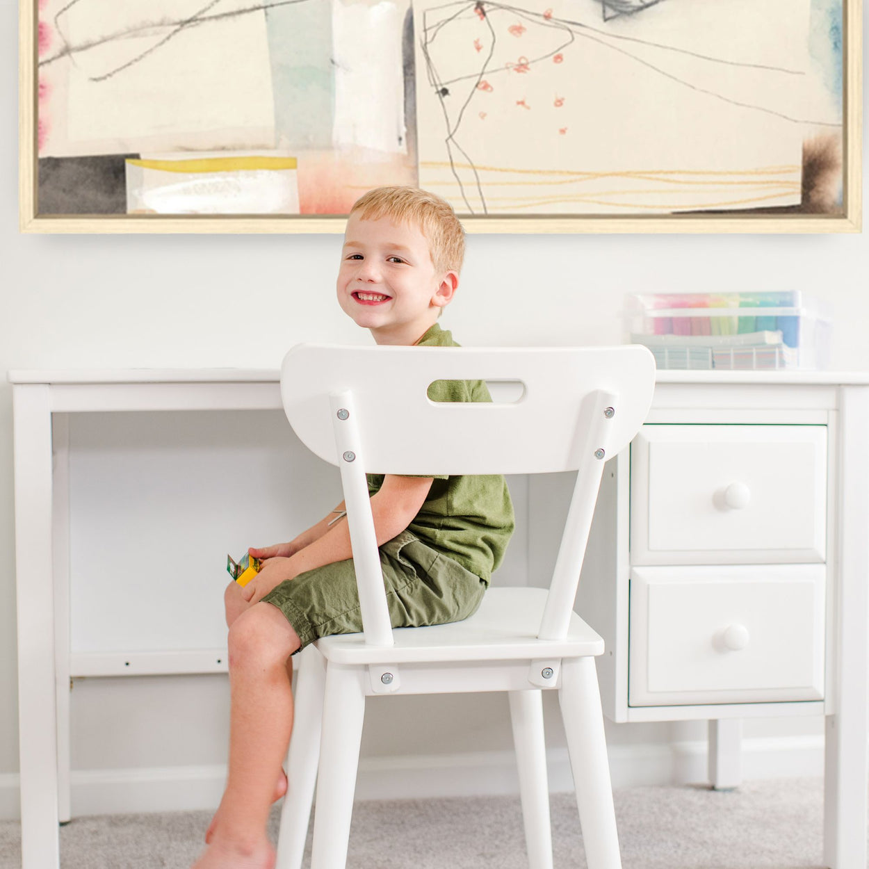 Happy child sitting at a white desk in a creative playroom.