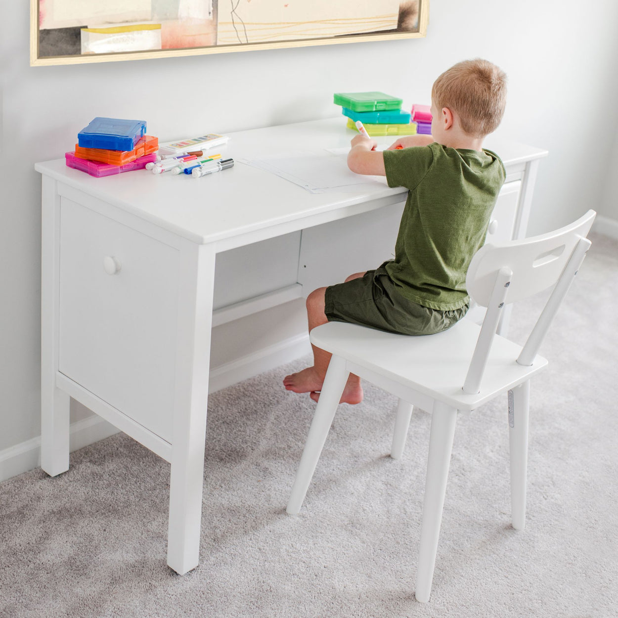 Child sitting at a white study desk with art supplies, engaging in creative drawing activities.
