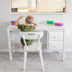 Young child sitting at a white desk engaging in creative play with colorful building blocks in a bright room.