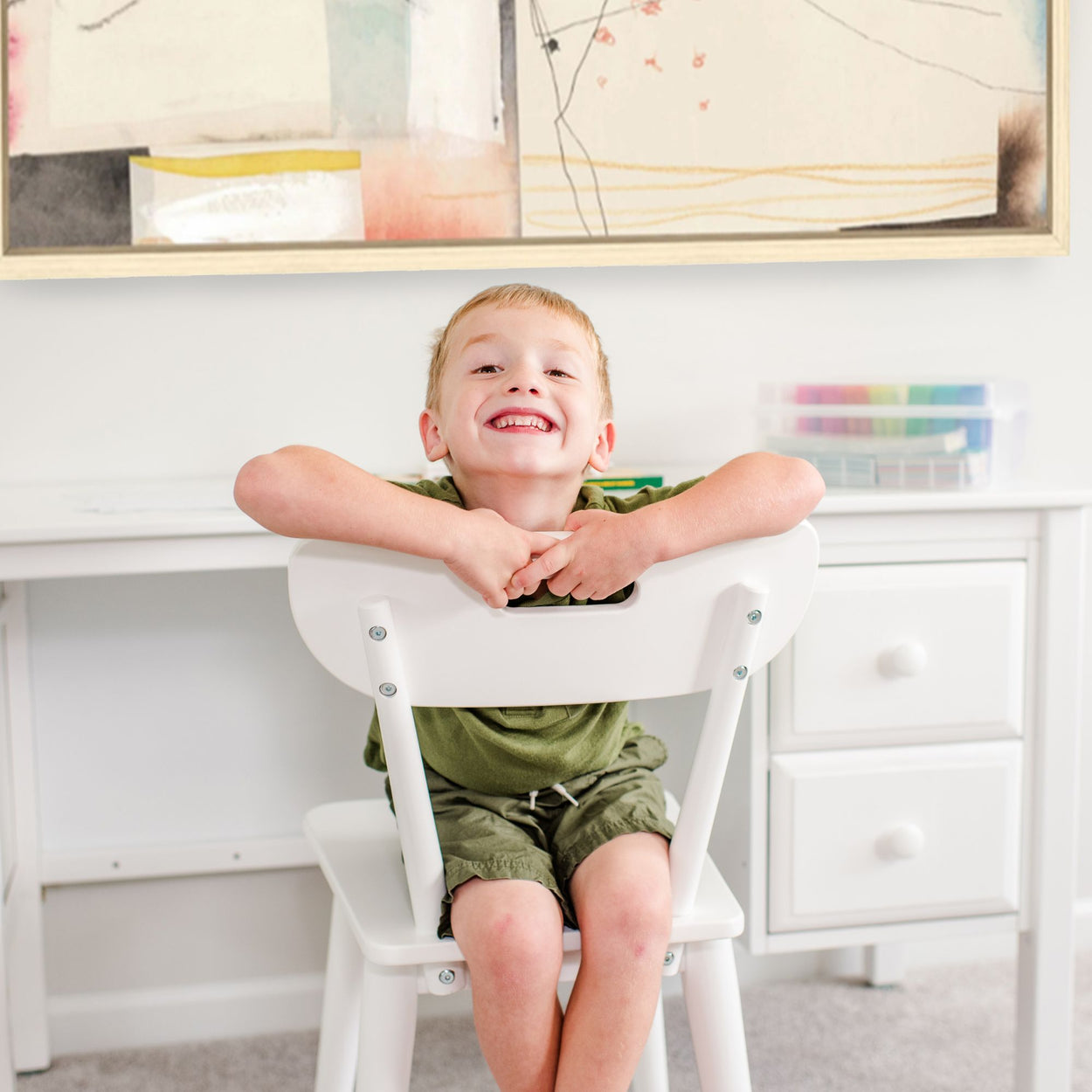 Child smiling while sitting on a white chair in a bright and modern children's study room.