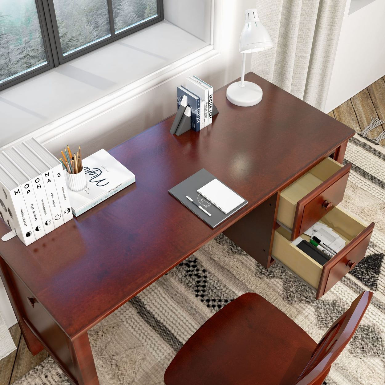 Modern wooden office desk with open drawers, white lamp, and organized stationery near a window.