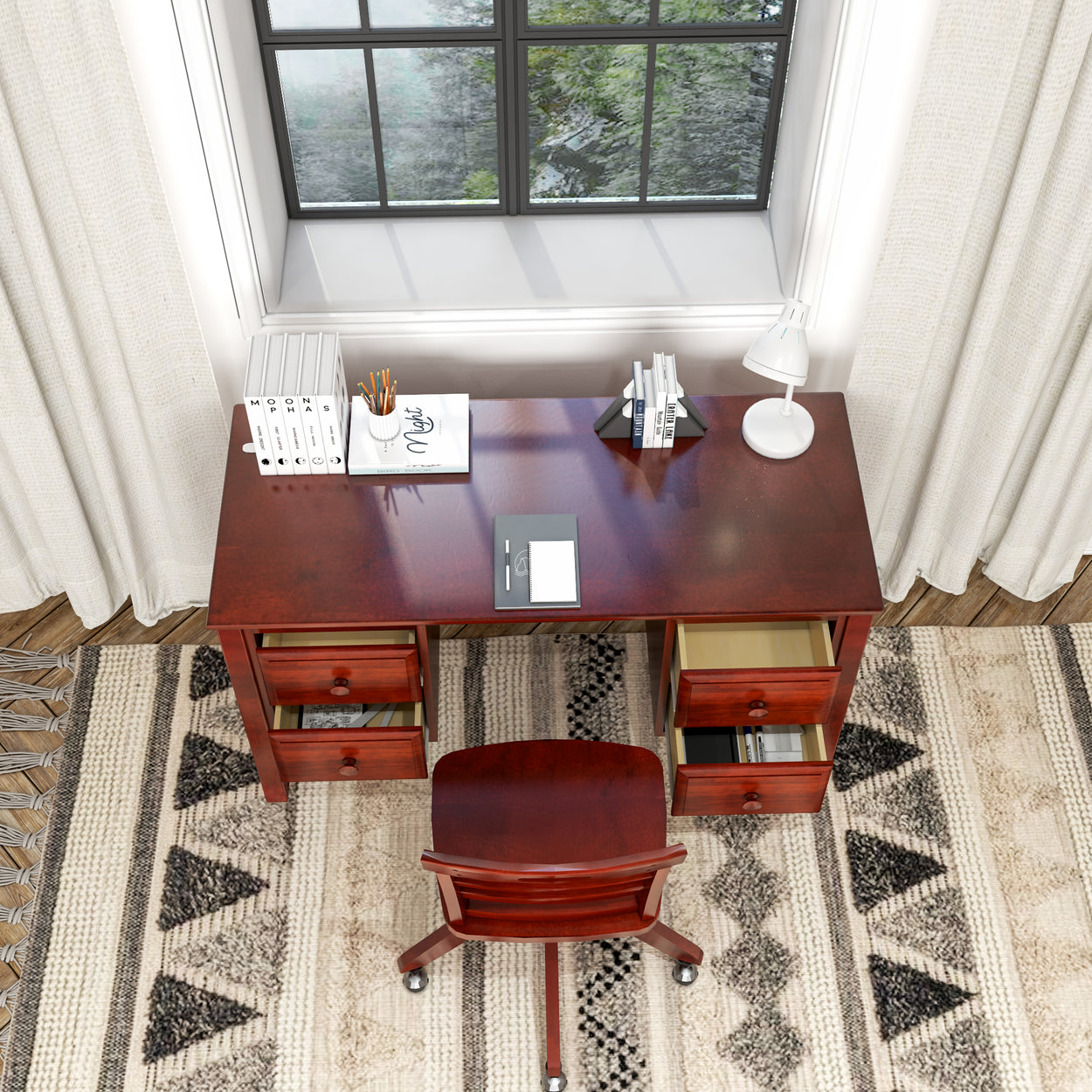 Cozy home office setup with wooden desk and chair, featuring books, notebooks, and a lamp by a window.