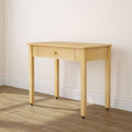 Light natural wood small writing desk with single centered drawer and round knob on caster feet, minimalist console table on hardwood floor against a white wall