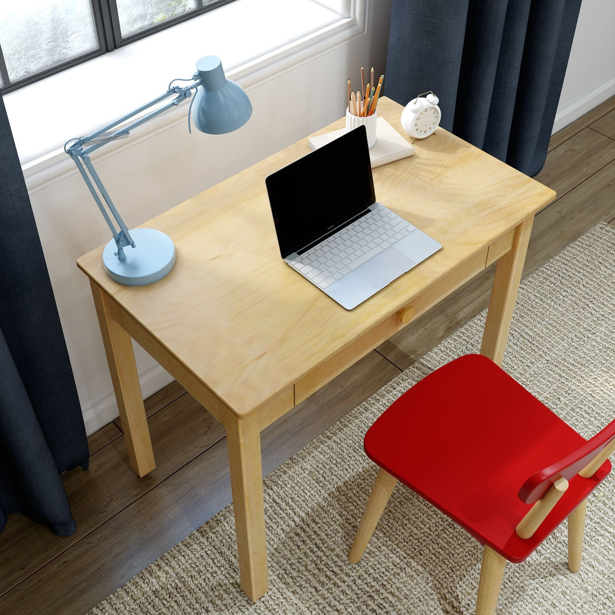 Minimal home office workspace with light wood desk, silver laptop, blue adjustable desk lamp, pencil cup, alarm clock and red chair by window