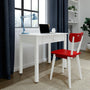 White wooden desk with drawer, red wooden chair, blue adjustable desk lamp and laptop by window with navy curtains in a modern minimalist small home office workspace