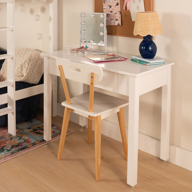 White kids vanity desk with Hollywood-style lighted mirror, navy ceramic lamp on books, two princess tiaras and wooden chair in children's bedroom