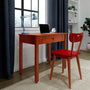 Wooden home office desk with laptop, blue desk lamp and red chair by window