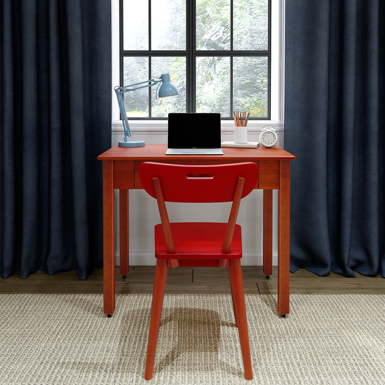 Modern home office workspace: red wooden desk and chair with laptop, blue desk lamp, pencil holder and alarm clock by window with dark curtains