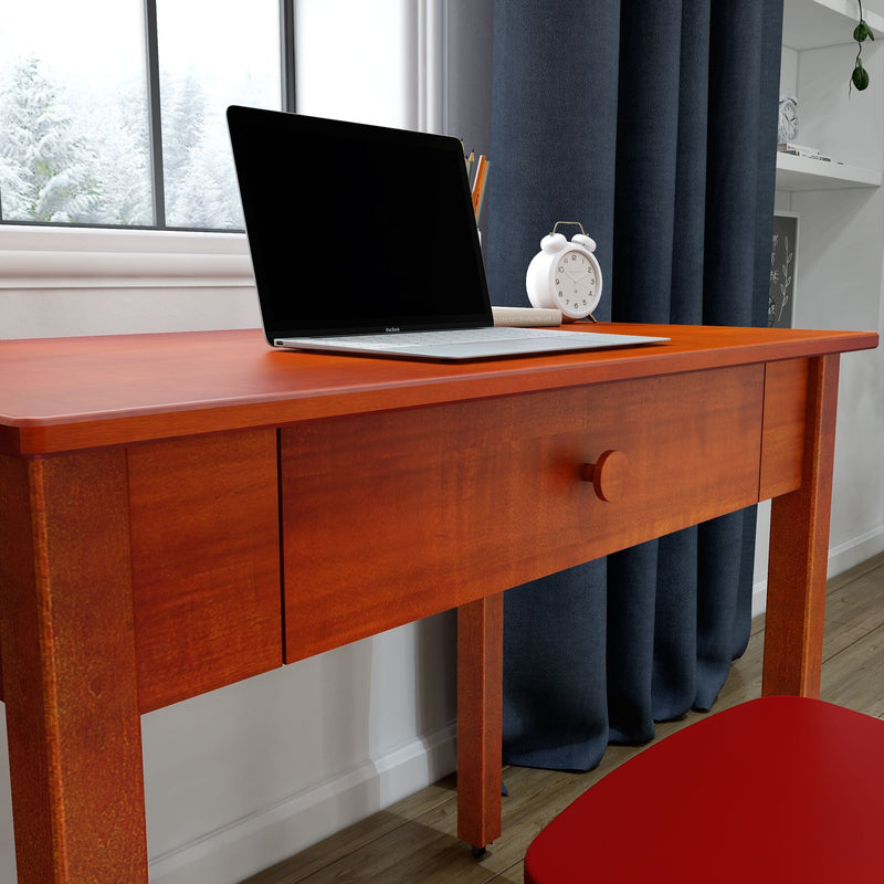 Red wooden desk with open laptop and white alarm clock beside a snowy window, cozy home office workspace with navy curtains and hardwood floor