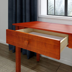 Cherry wood writing desk with open drawer in a modern home office by a window with snowy view, dark curtains and hardwood floor