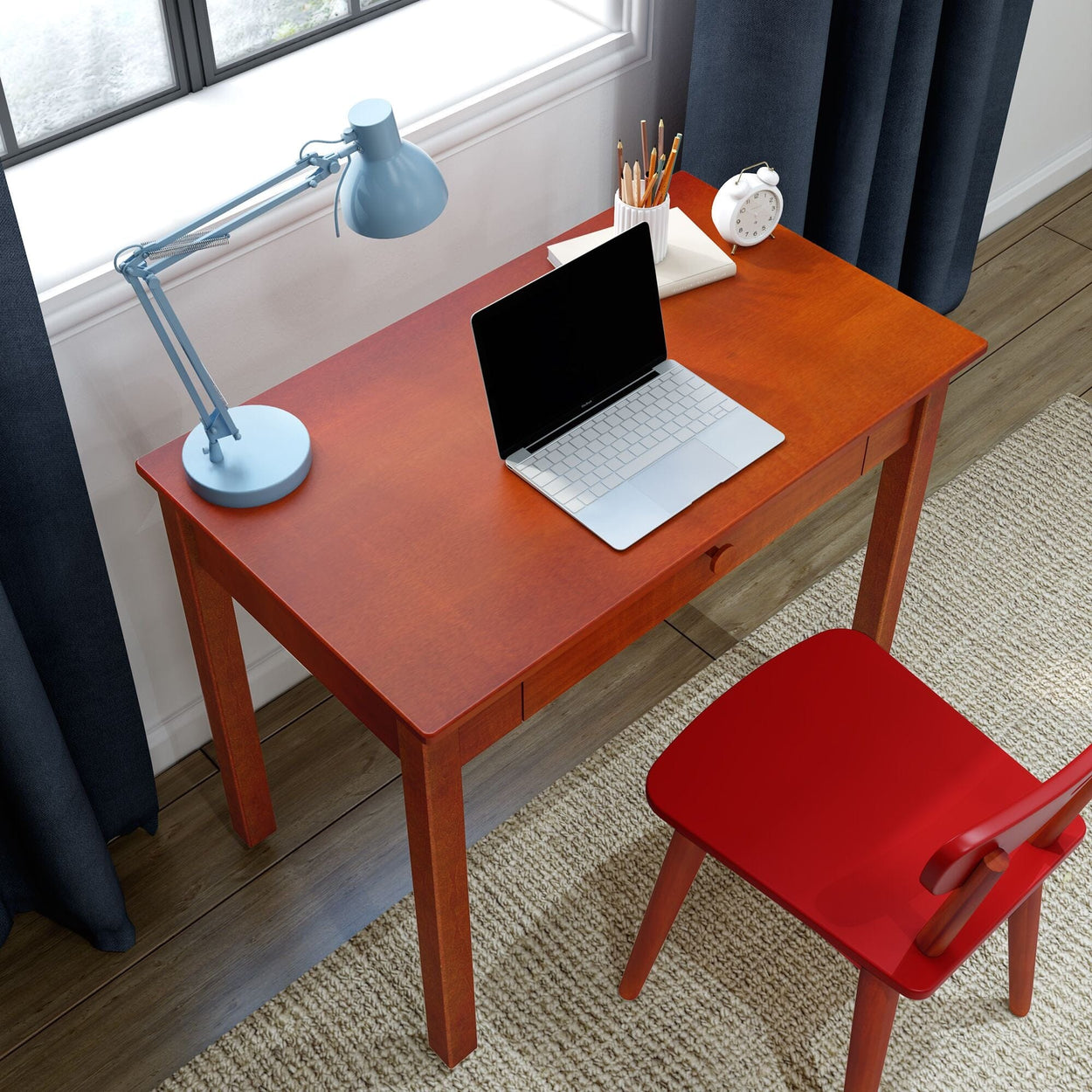 Cherry wood desk home office with laptop, blue adjustable lamp, pencil cup, white alarm clock and red chair by window