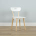 Minimalist Scandinavian white wooden dining chair with natural beech legs on light hardwood floor against a pale gray wall